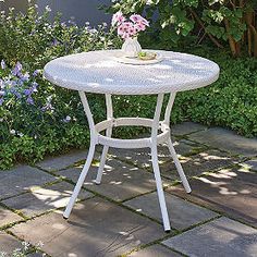 a small white table sitting in the middle of a garden with purple flowers on it