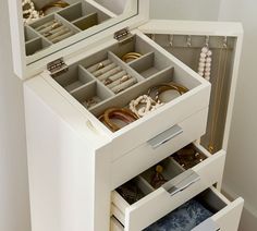 an open jewelry box sitting on top of a white floor next to a mirror and wall