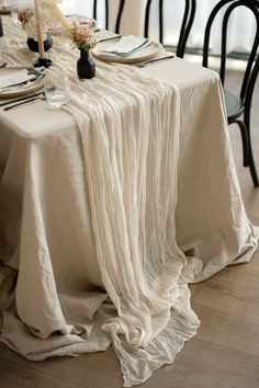 the table is set with white linens and place settings for two people to eat