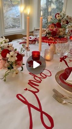 the table is set with red and white flowers, silverware, candles, and napkins