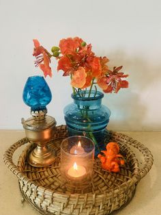 a wicker tray with candles and flowers in it on a counter top next to a blue glass vase