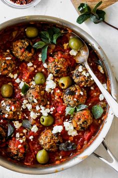 a pan filled with meatballs and olives on top of a white countertop