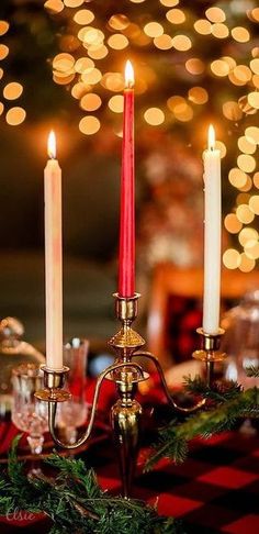 three lit candles are sitting on a table with christmas decorations and lights in the background