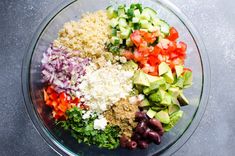 the ingredients for this salad are mixed together in a large glass bowl, including olives, tomatoes, cucumbers, and other vegetables