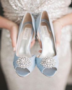 a woman holding two pairs of blue high heel shoes with jeweled decorations on them