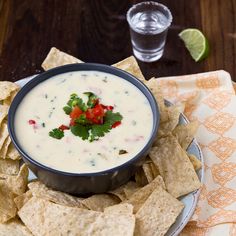 a bowl of white quesadilla dip surrounded by tortilla chips and cilantro