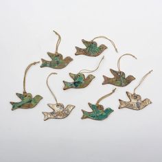 six metal birds hanging from strings on a white surface with green and gold accents,