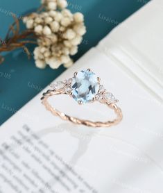 an oval blue topaz ring with three pear shaped diamonds in front of a book