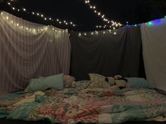 an unmade bed with pillows and blankets on it in front of some string lights