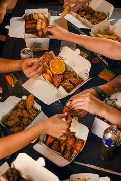 several people are eating food from boxes on a table with oranges and other foods