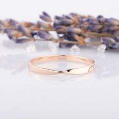 a rose gold wedding ring sitting next to lavender flowers