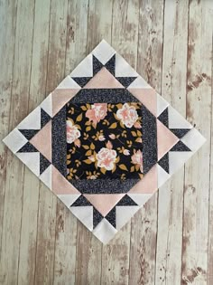 a black and pink patchwork square with flowers on it sitting on a wooden surface