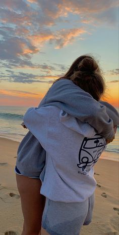 a woman is walking on the beach with her back to the camera and she's wearing a hoodie