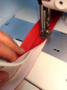 a person is using a sewing machine to sew something red and white on the table