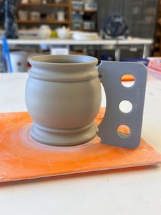 a white vase sitting on top of an orange place mat next to a gray cup