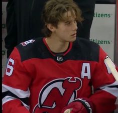 a hockey player sitting on the bench with his hands in his pockets and wearing gloves