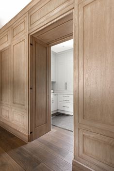 an open door leading to a kitchen with white cabinets and wood flooring on the walls