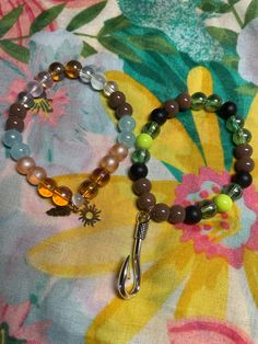 two bracelets with beads and charms on a flowered cloth background, one has a spoon