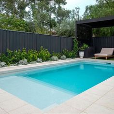 an empty swimming pool in the middle of a backyard with a lounge chair and privacy fence