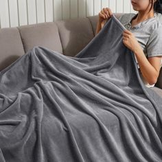 a woman sitting on a couch holding up a gray blanket