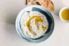 a bowl of hummus and pita bread on a white table with olive oil