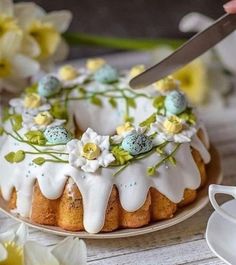 a cake with white icing and flowers on it next to a cup of tea