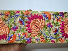 a hand is holding a piece of fabric with flowers on it and green, orange, pink, blue, and yellow colors