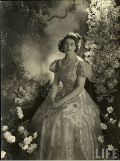 an old photo of a woman in a dress sitting on a bench with flowers around her