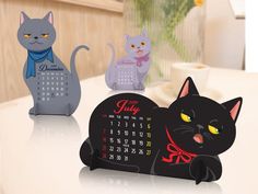 three cat shaped desk calendars sitting on top of a table next to each other