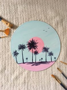 a painted plate with palm trees on it and paintbrushes next to the painting