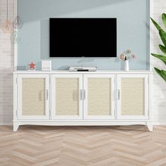 a flat screen tv sitting on top of a white cabinet next to a potted plant