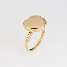 This is part of Chairish’s Fine Jewelry assortment.  Stylish picture locket ring crafted in 14 karat yellow gold.   The heart shaped ring is a wonderful sentimental piece. The locket opens to reveal two sections that can accommodate a picture or keepsake. The low rise ring (5mm - 0.19 inches) sits comfortably on the finger.  The ring is in very good condition and was recently professionally cleaned and polished.   Particulars:  Weight: 3.3 grams  Stones:  N/A   Size & Measurements: The ring is a Yellow Gold Oval Heart Ring For Valentine's Day, Yellow Gold Heart-shaped Engraved Ring, Engraved Heart-shaped Yellow Gold Ring, Engraved Heart Shaped Yellow Gold Ring, Heart-shaped Yellow Gold Signet Ring Stamped 14k, Yellow Gold Heart-shaped Engraved Ring Stamped 14k, Yellow Gold Heart Shaped Signet Ring Stamped 14k, Heart-shaped Engraved Yellow Gold Ring Stamped 14k, 14k Yellow Gold Heart Engraved Ring