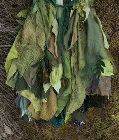 a pile of green and brown fabric hanging from the side of a forest floor next to trees