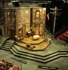 an empty stage with chairs and tables in front of a building that looks like it is set for a play