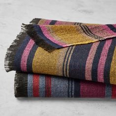 two blankets folded on top of each other in different colors and patterns with fringes