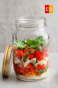 a glass jar filled with lots of different types of vegetables and herbs on top of a table