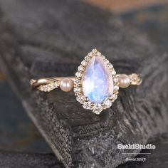 an engagement ring with a pear shaped blue stone surrounded by diamonds and pearls on a rock