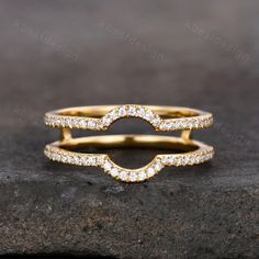 two gold wedding rings with diamonds on top of each other, sitting on a rock