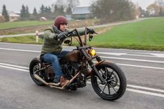 a man riding on the back of a brown motorcycle down a street next to a lush green field