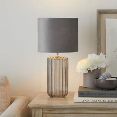 a lamp on a table next to a book and a vase with flowers in it