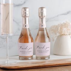 two bottles of champagne sitting on a table next to a wine glass and vase with flowers