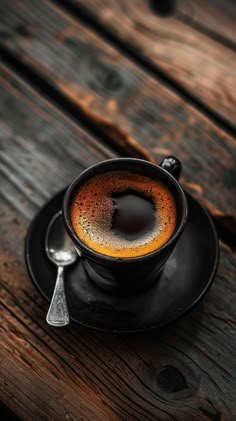 a cup of coffee sitting on top of a black saucer next to a spoon