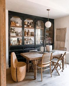 a dining room table with chairs and shelves in the back ground, filled with dishes