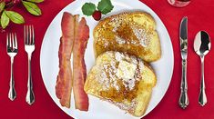 two pieces of french toast and bacon on a plate with silverware next to it