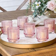 six pink glass cups on a tray with flowers in the backgroung behind them