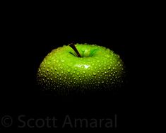 an apple with drops of water on it in the dark, against a black background