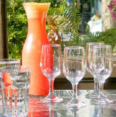 a table topped with lots of glasses next to a vase filled with flowers and greenery