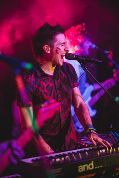 a man that is standing up with a keyboard in front of him and singing into a microphone