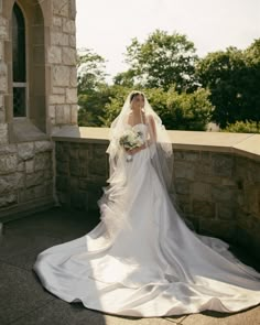 a woman in a wedding dress standing on a stone wall with her veil blowing in the wind