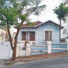 a blue and white house sitting next to a tree on the side of a road